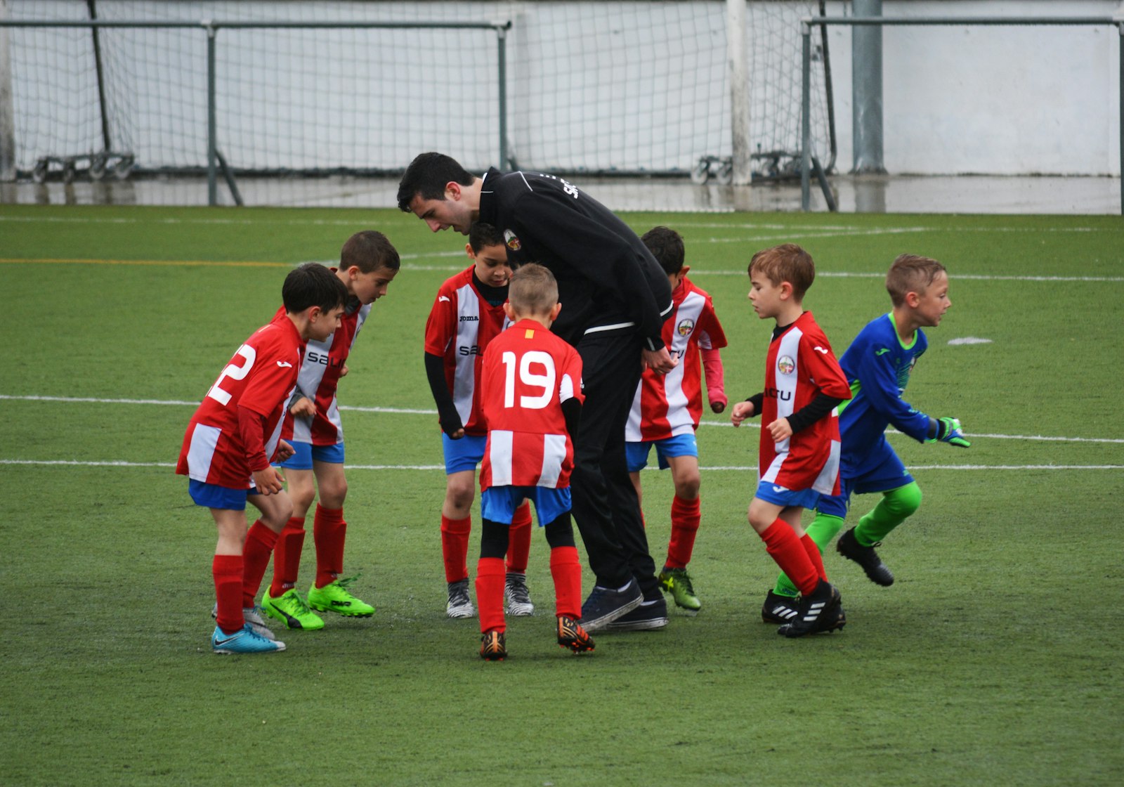 Kids huddled around their coach on a community soccer pitch.